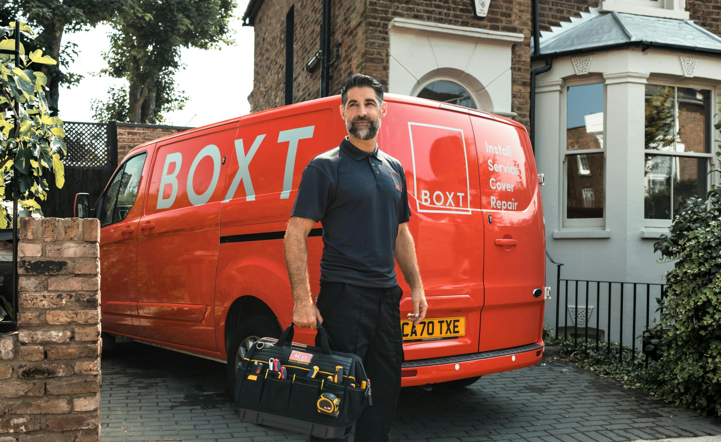 a BOXT engineer holding a tool bag, stood in front of a coral BOXT branded van