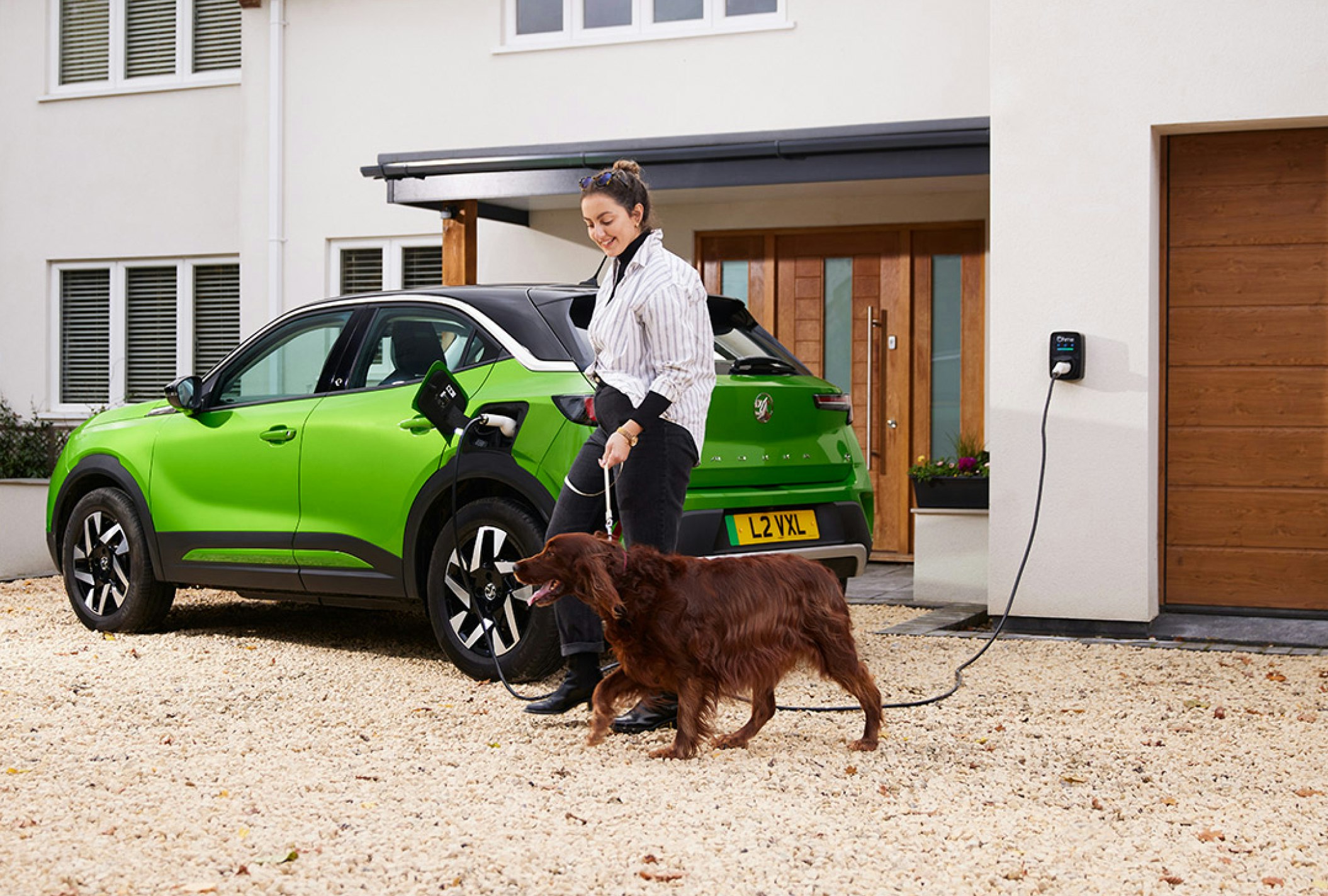 lady walking her dog past her charging car in front of her home