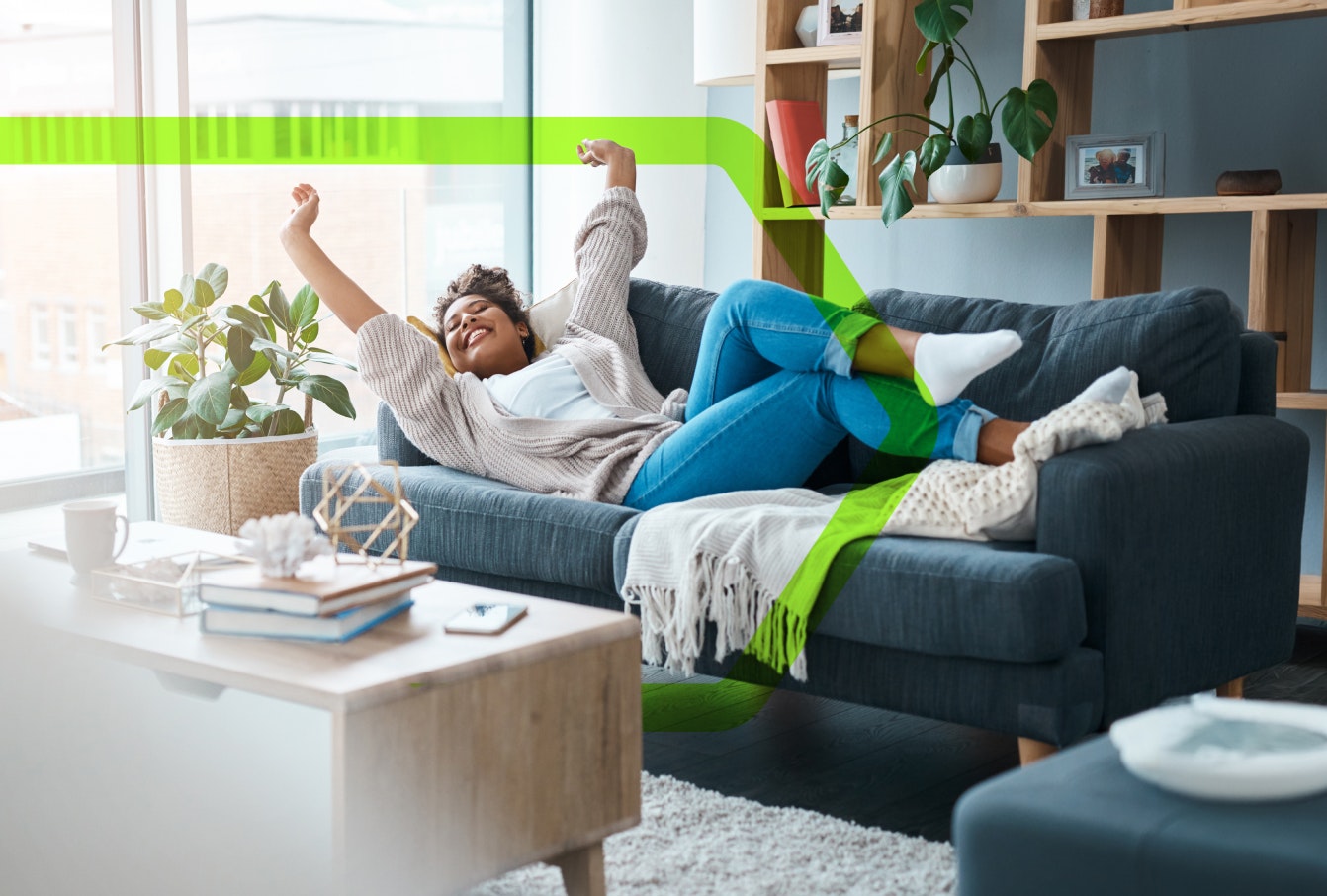 a happy woman, laying on the sofa in her cosy looking flat, with her arms raised in celebration