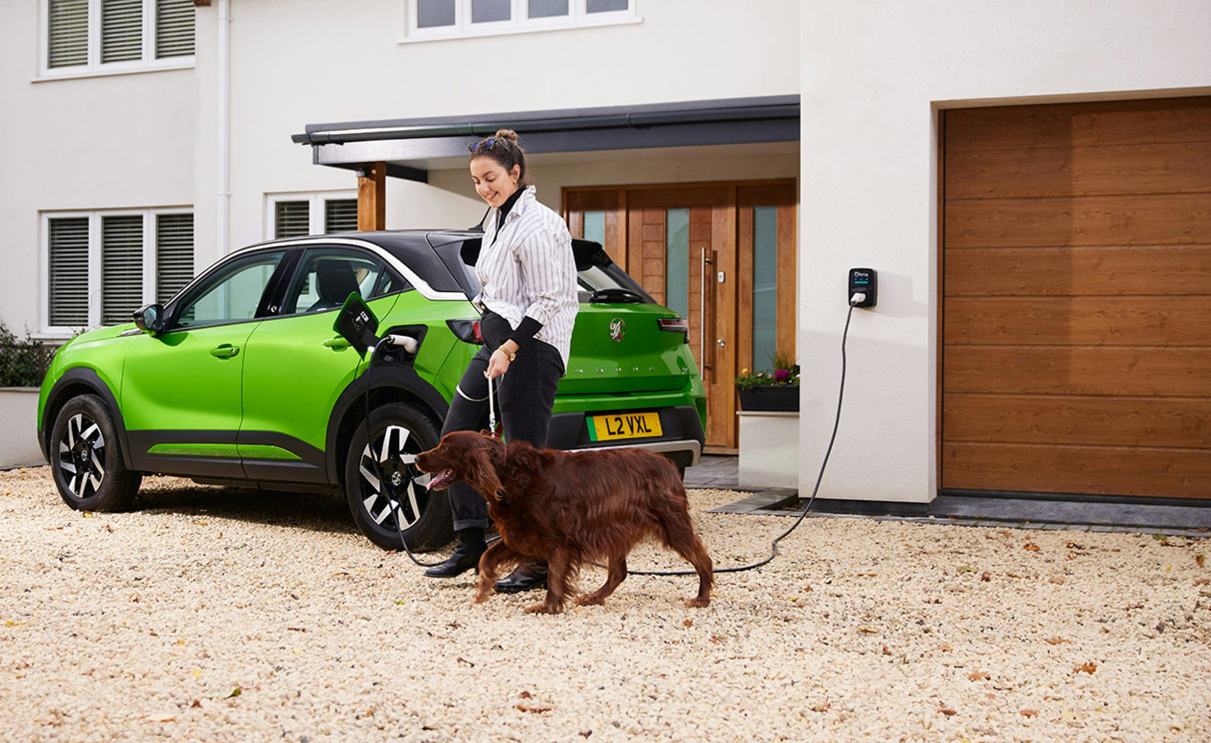 lady walking her dog past her charging car in front of her home