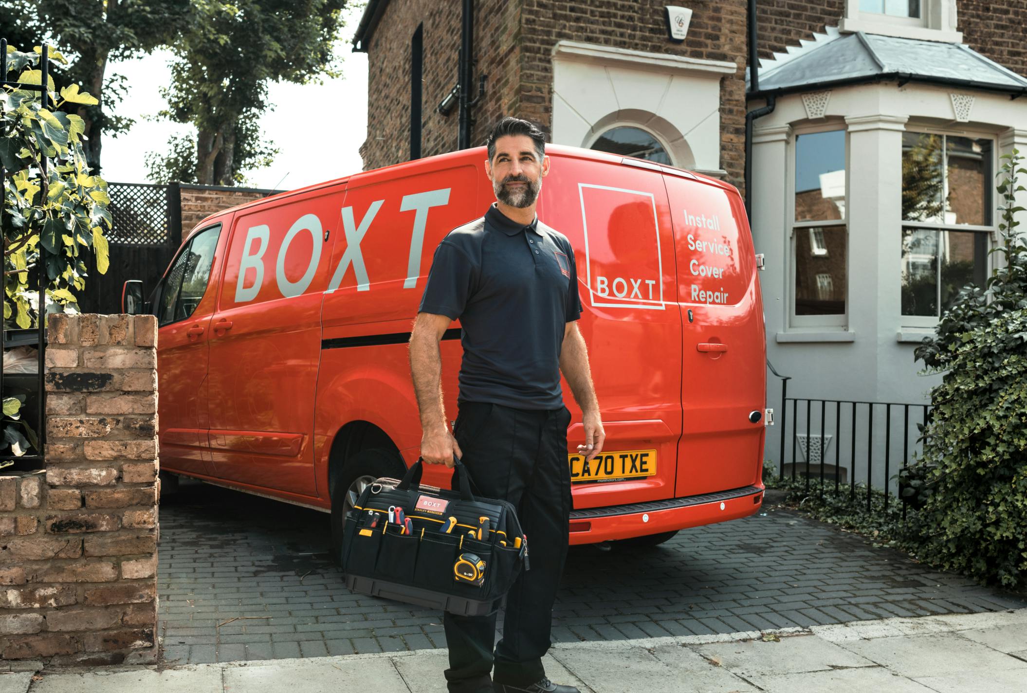 a BOXT engineer holding a tool bag, stood in front of a coral BOXT branded van