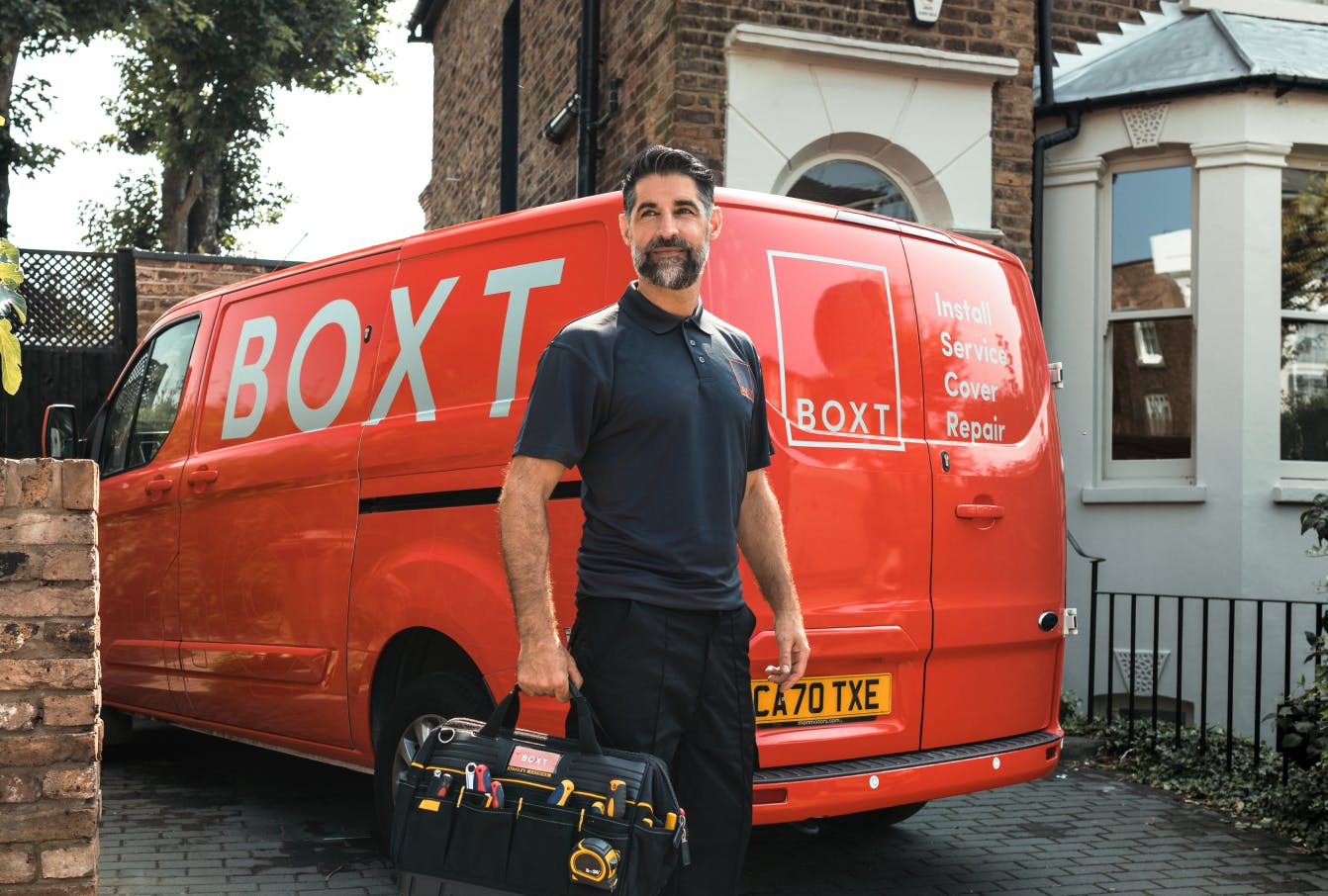 a BOXT engineer holding a tool bag, stood in front of a coral BOXT branded van