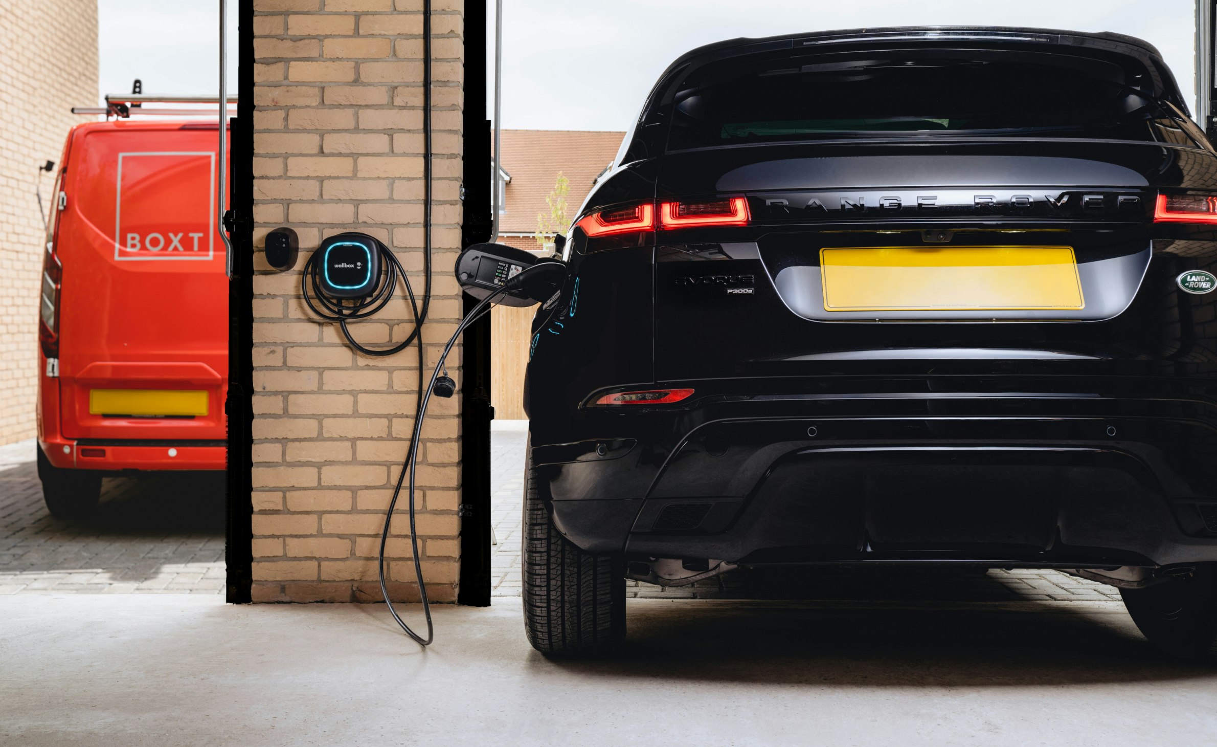 A black range rover charging in a garage, with a boxt van parked outside