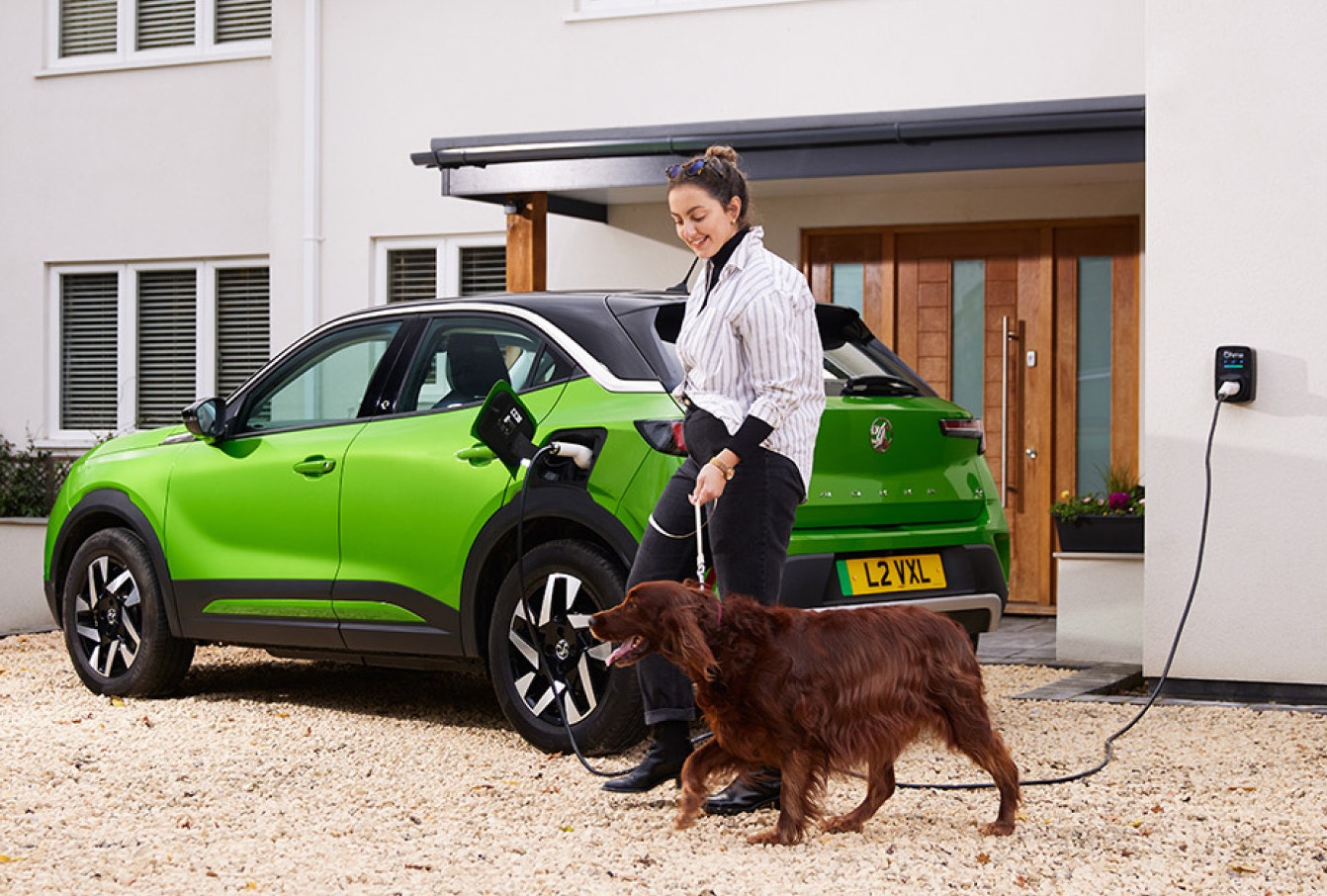 lady walking her dog past her charging car in front of her home