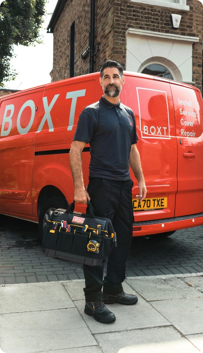 A BOXT engineer holding a toolkit stood in front of a BOXT van outside a customers property 