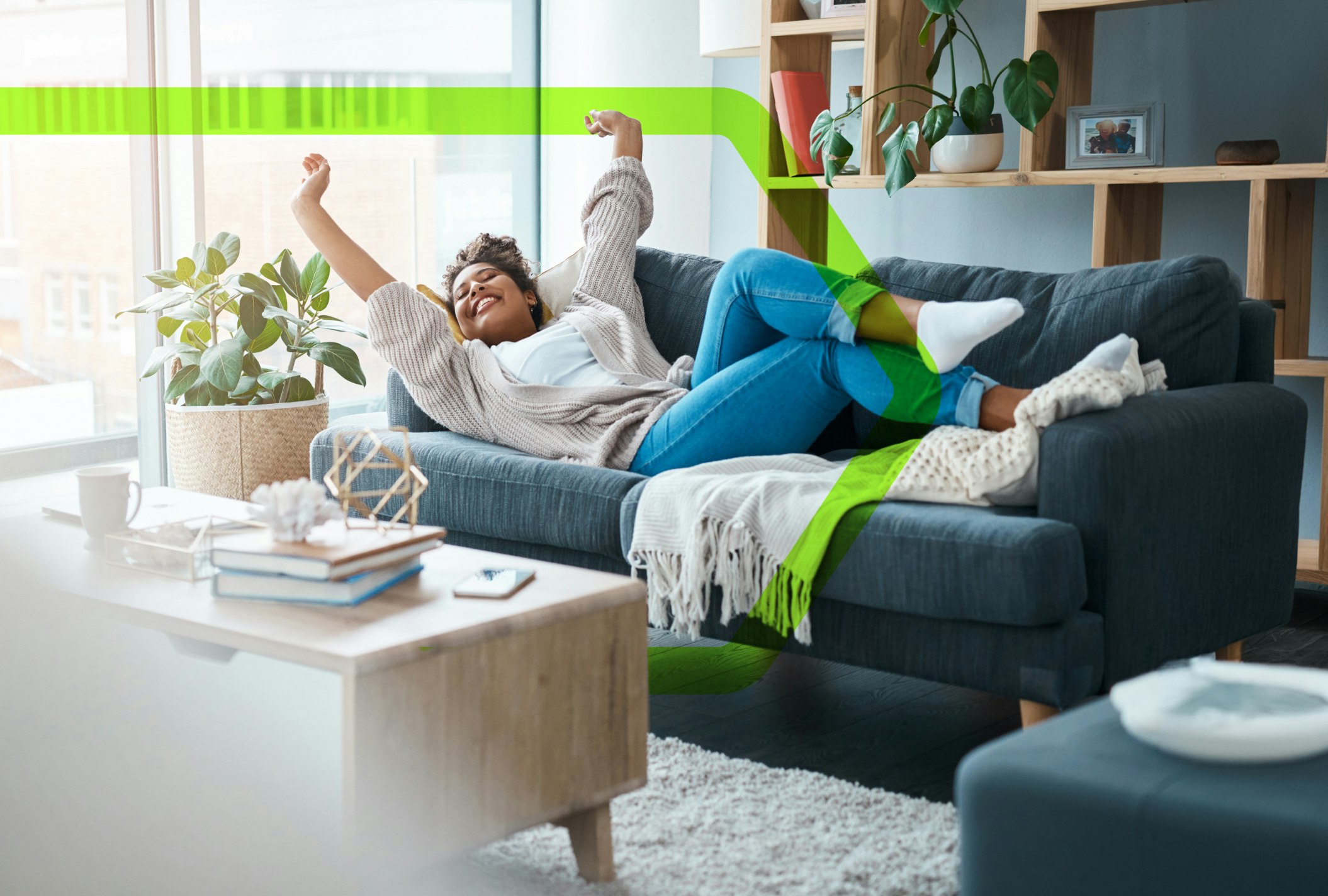 a happy woman, laying on the sofa in her cosy looking flat, with her arms raised in celebration