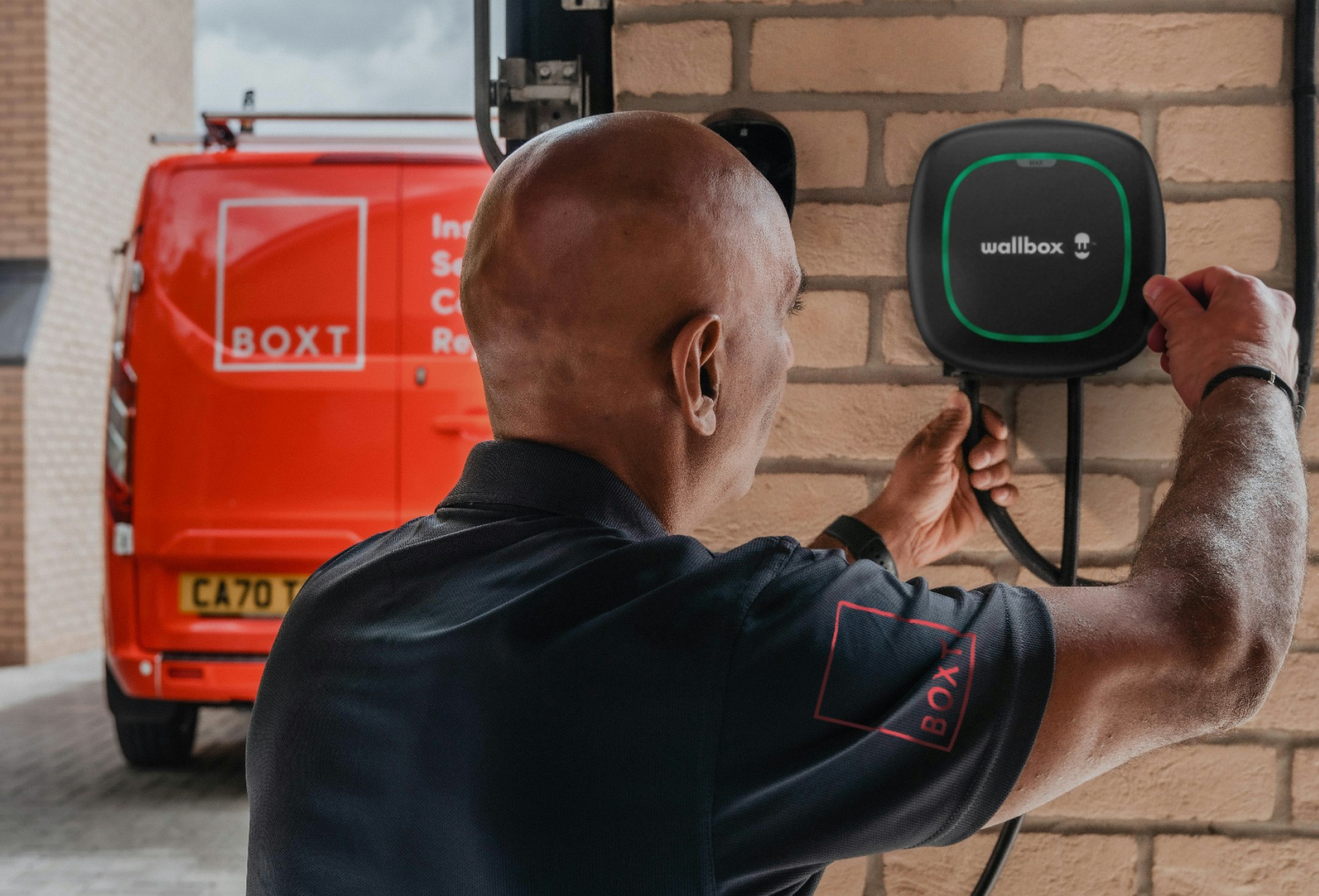 a BOXT engineer installing an EV Charger, with a red BOXT-branded van visible in the background