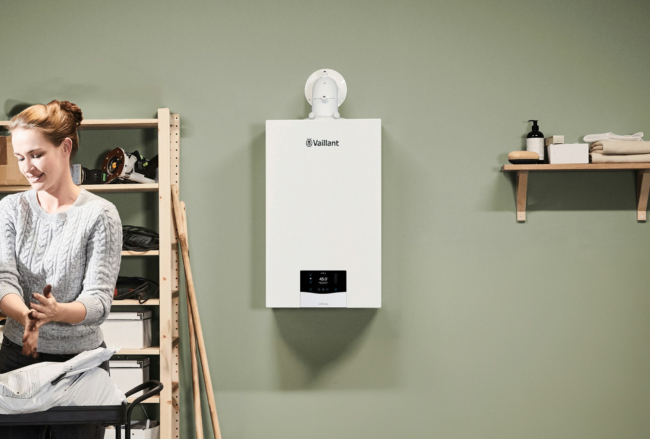 A Vaillant boiler installed on a green wall, with a smiling woman to the side of the image