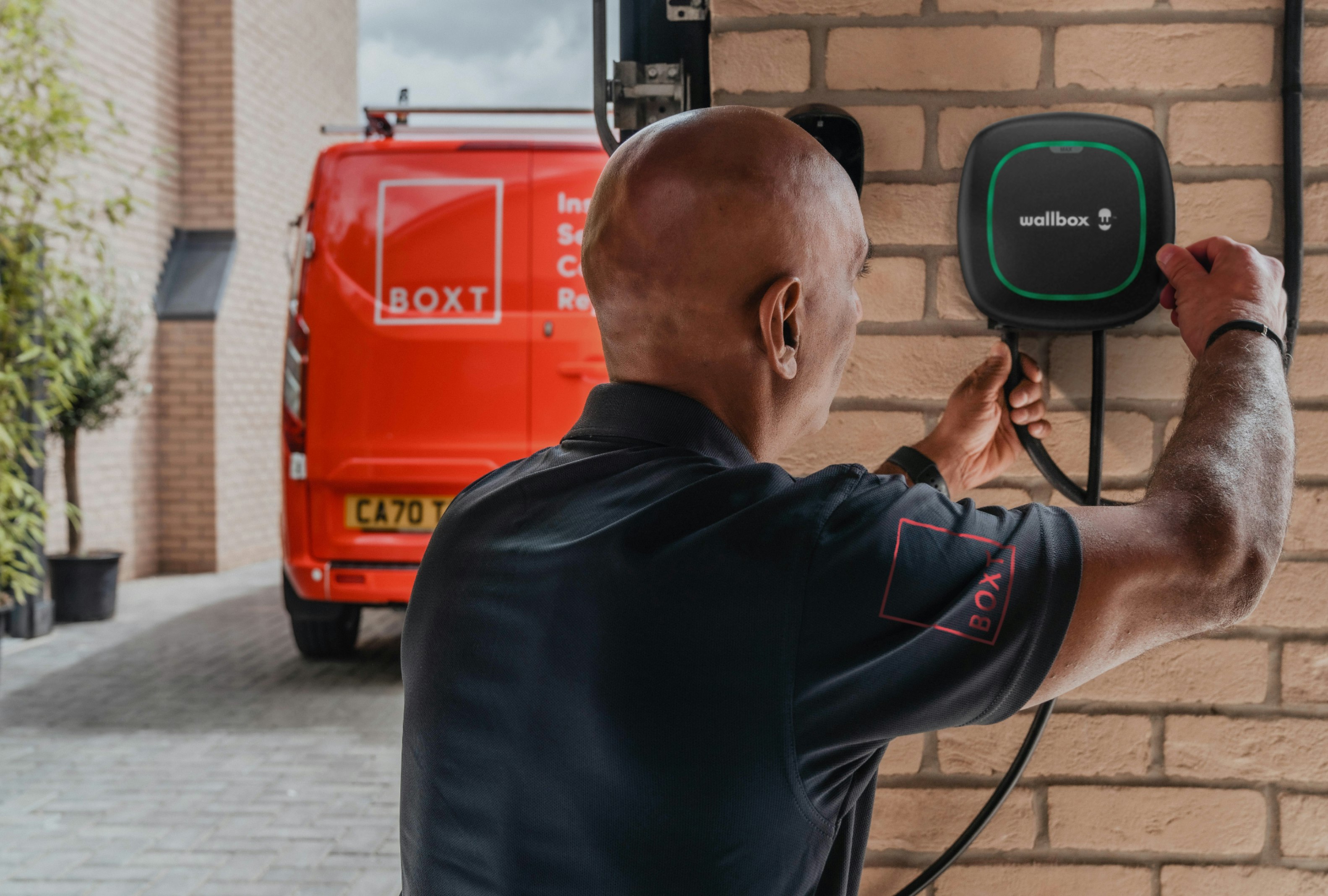 a BOXT engineer installing an EV Charger, with a red BOXT-branded van visible in the background