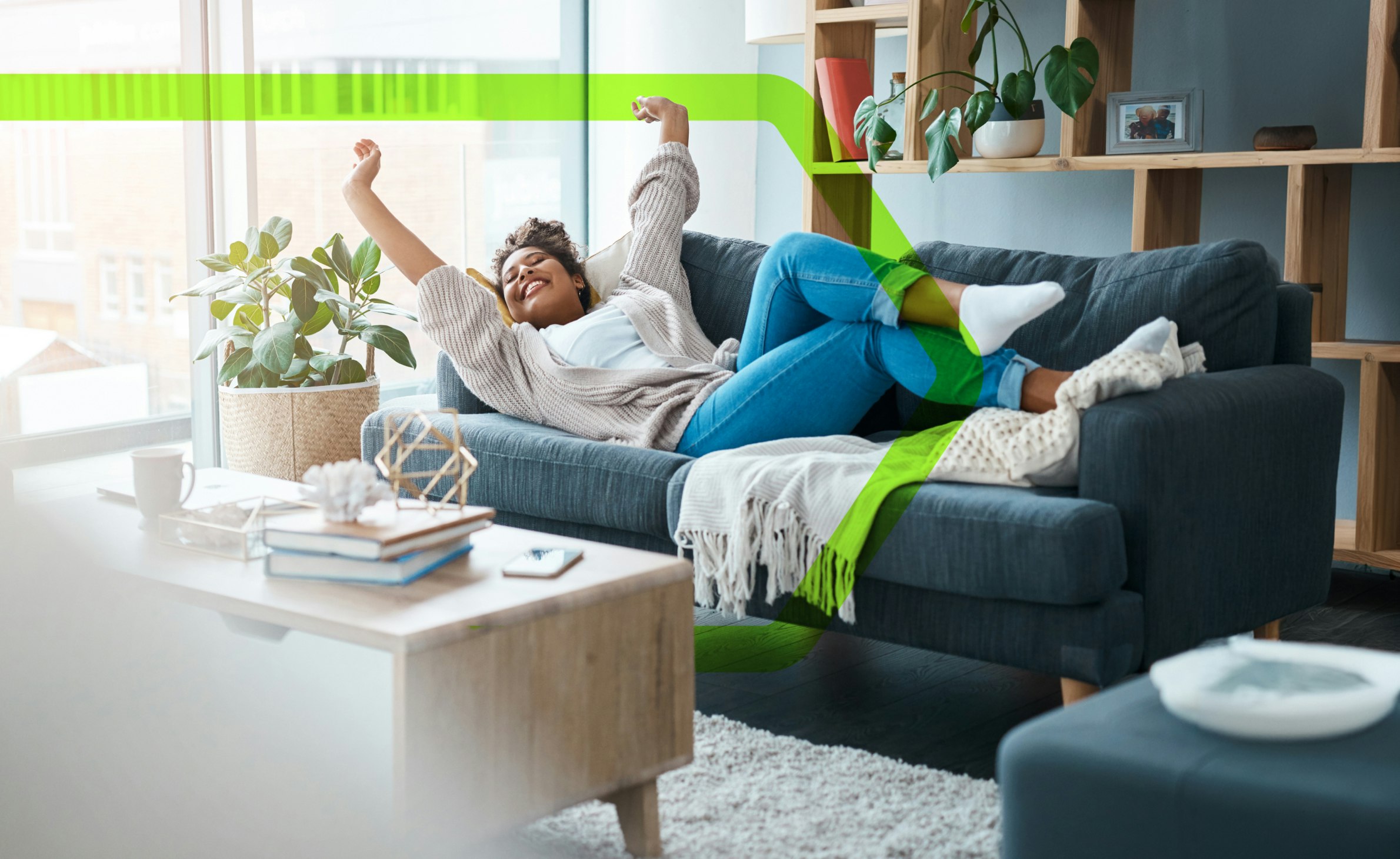 a happy woman, laying on the sofa in her cosy looking flat, with her arms raised in celebration