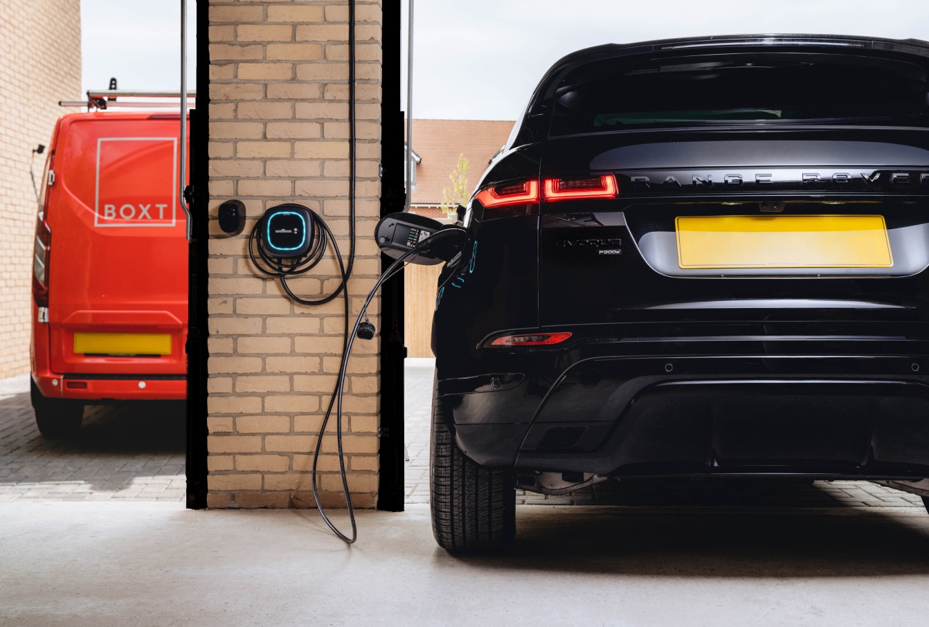 A black range rover charging in a garage, with a boxt van parked outside