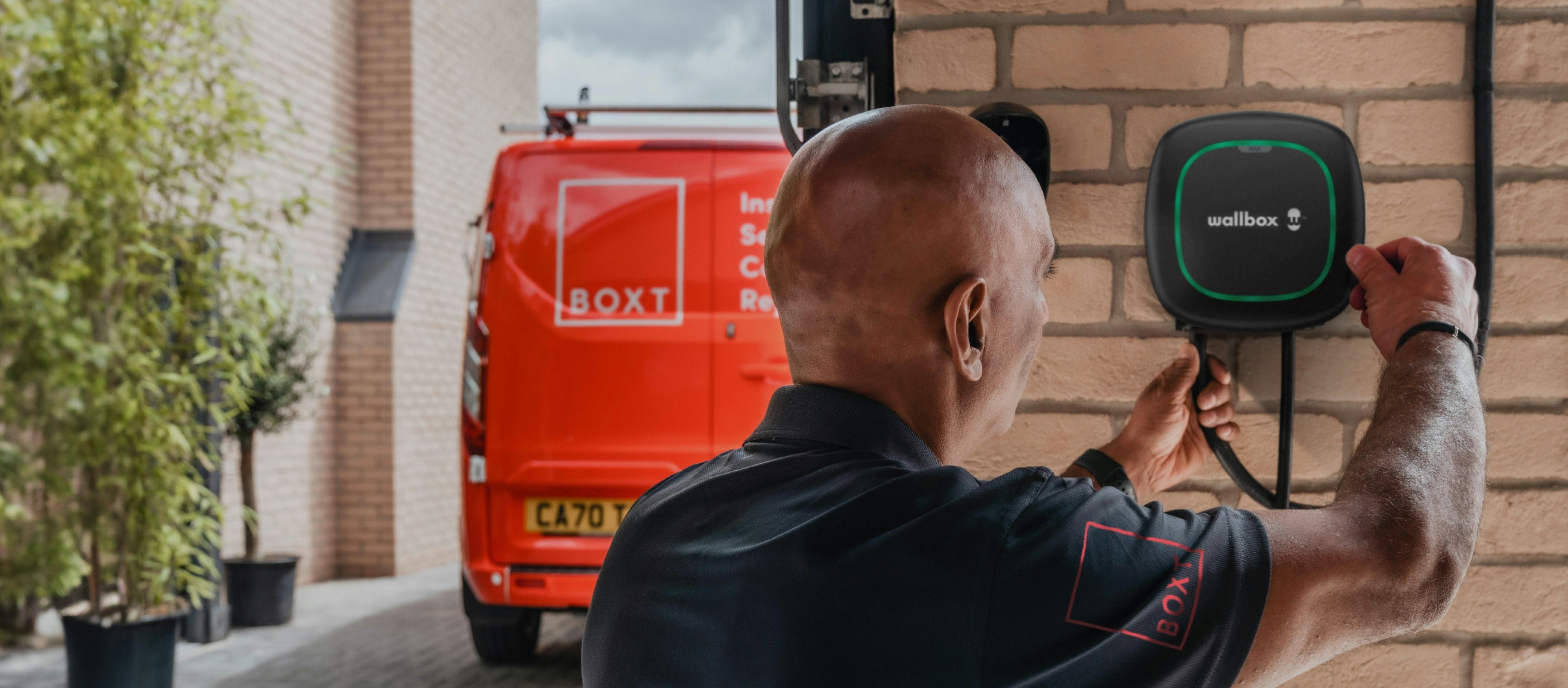 a BOXT engineer installing an EV Charger, with a red BOXT-branded van visible in the background