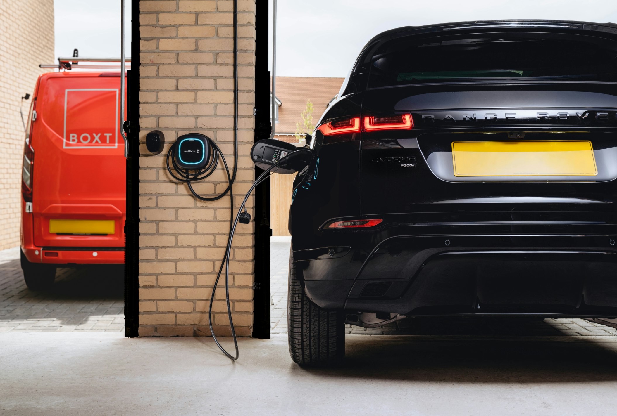 A black range rover charging in a garage, with a boxt van parked outside